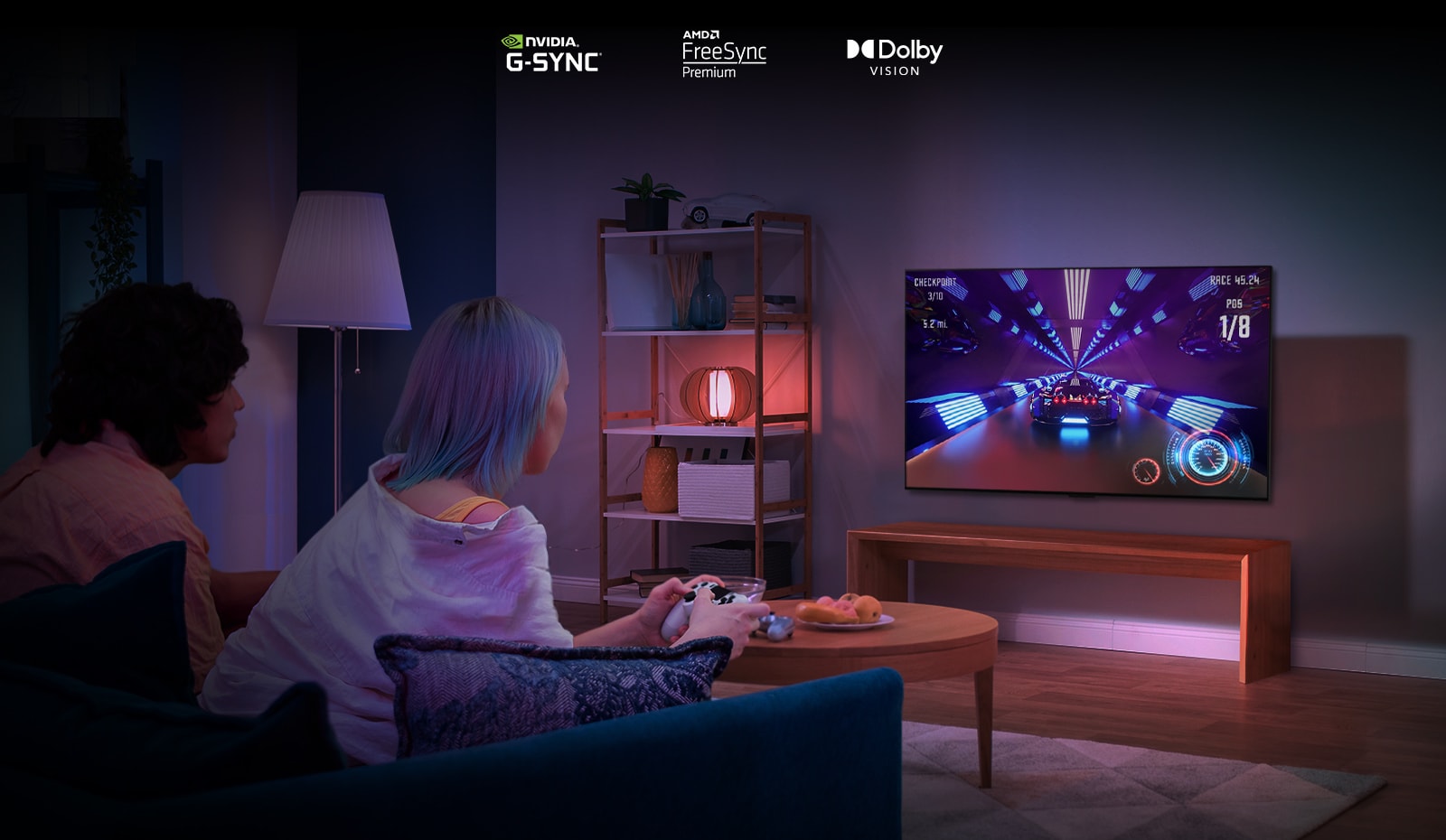 Two people sit on a couch playing a racing game with a controller and LG OLED G2 in a living room.